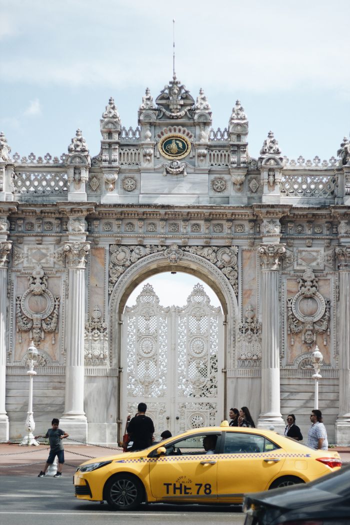 A vibrant yellow taxi passes in front of the ornate Dolmabahçe Palace gate in Istanbul, Turkey.