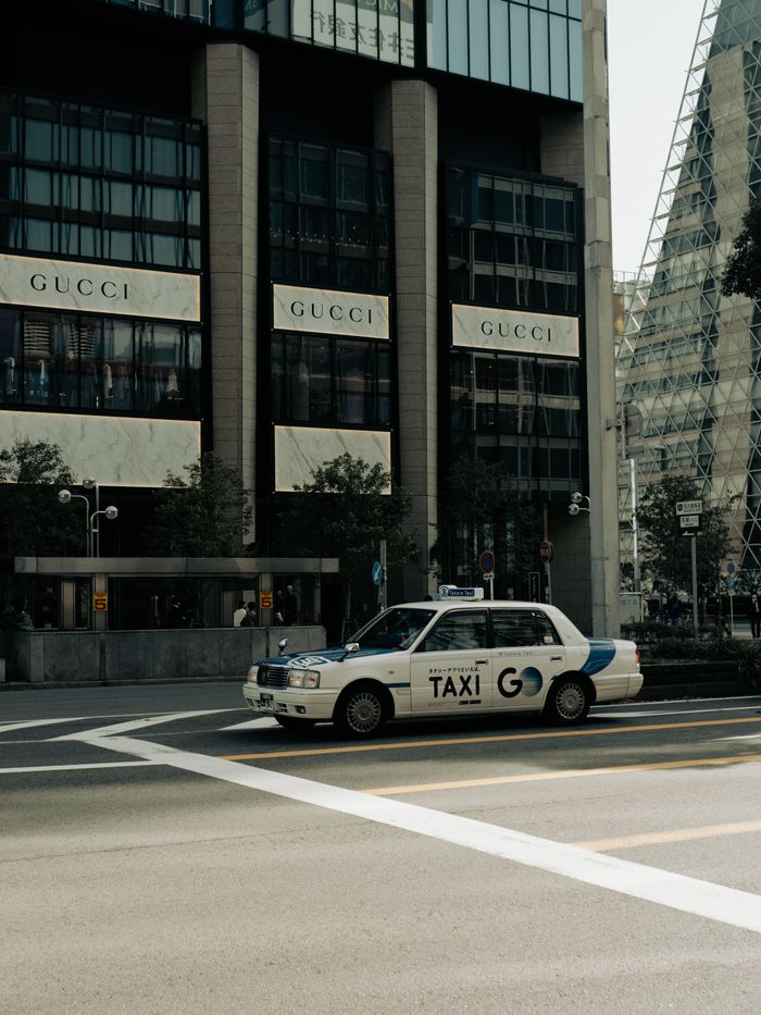 Taxi passing by Gucci storefront in bustling Nagoya street.