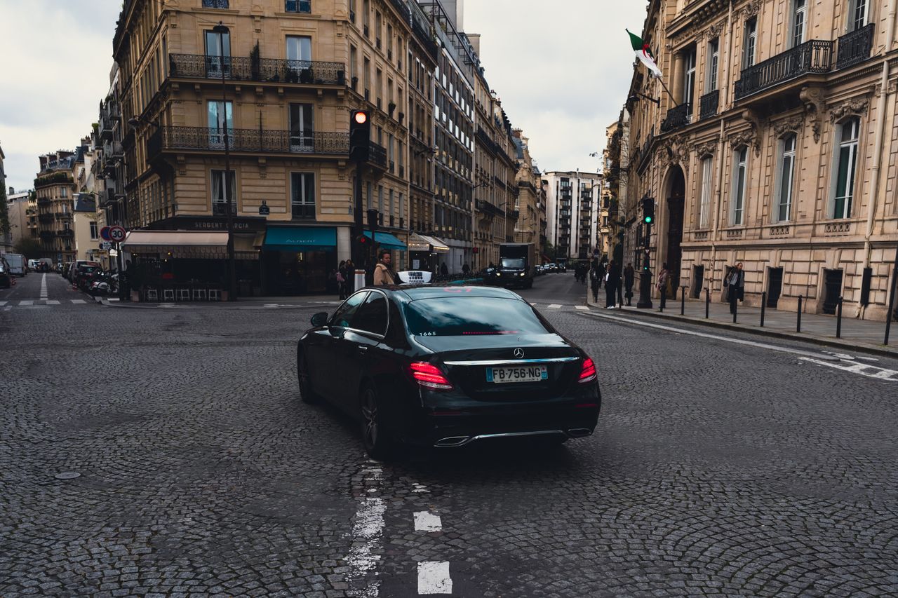 hero-img-02 Elegant black Mercedes-Benz taxi driving through charming Paris streets, highlighting urban sophistication.