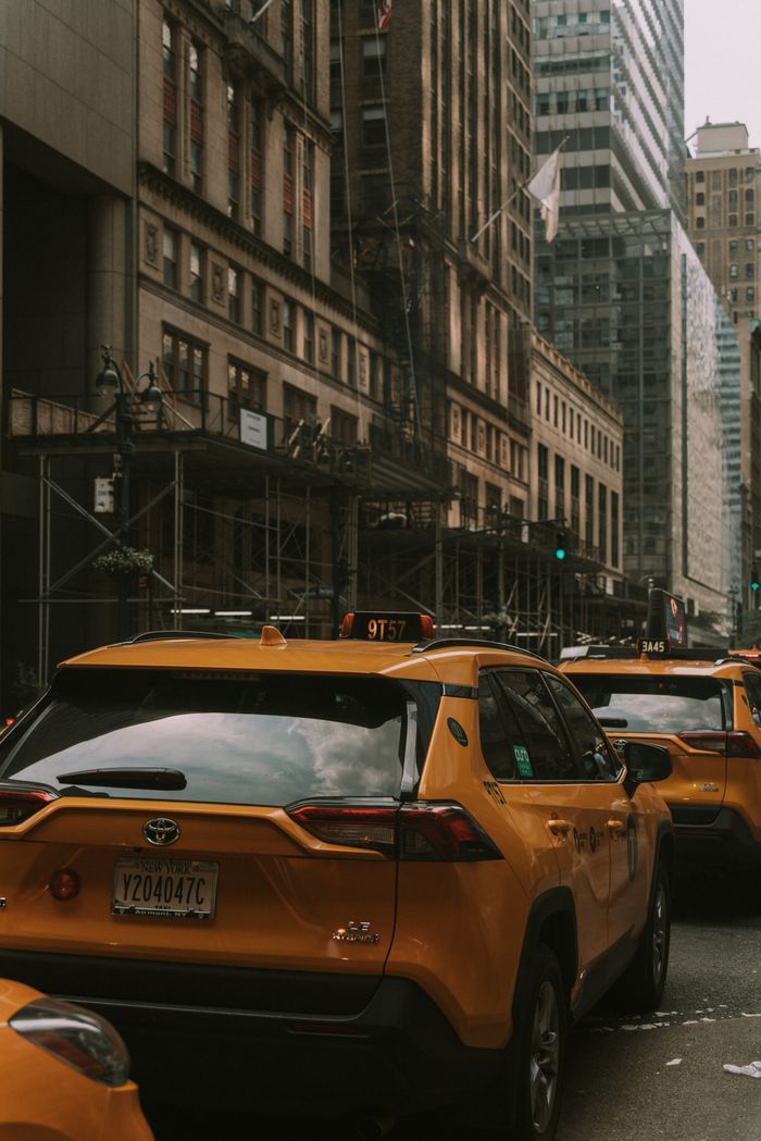 gallery-6 A busy street scene featuring iconic yellow taxis and tall city buildings in an urban setting.
