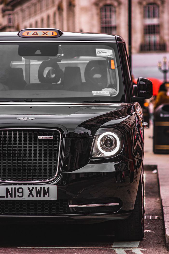 contact-img Front view of a classic black taxi parked on a city street highlighting urban elegance.
